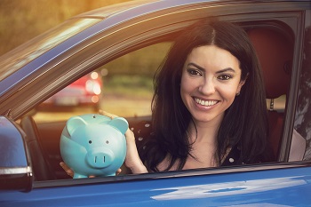 Fazit: Autobank oder Hausbank? Lächelnde Frau sitzt mit Sparschwein im Auto